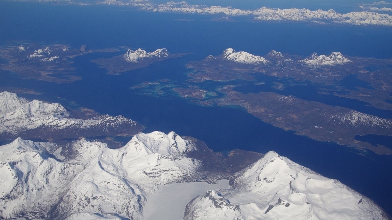 Nous survolons les fjords où la mer est encore prise par les glaces et les sommets très enneigés. Vol Oslo - îles Lofoten
